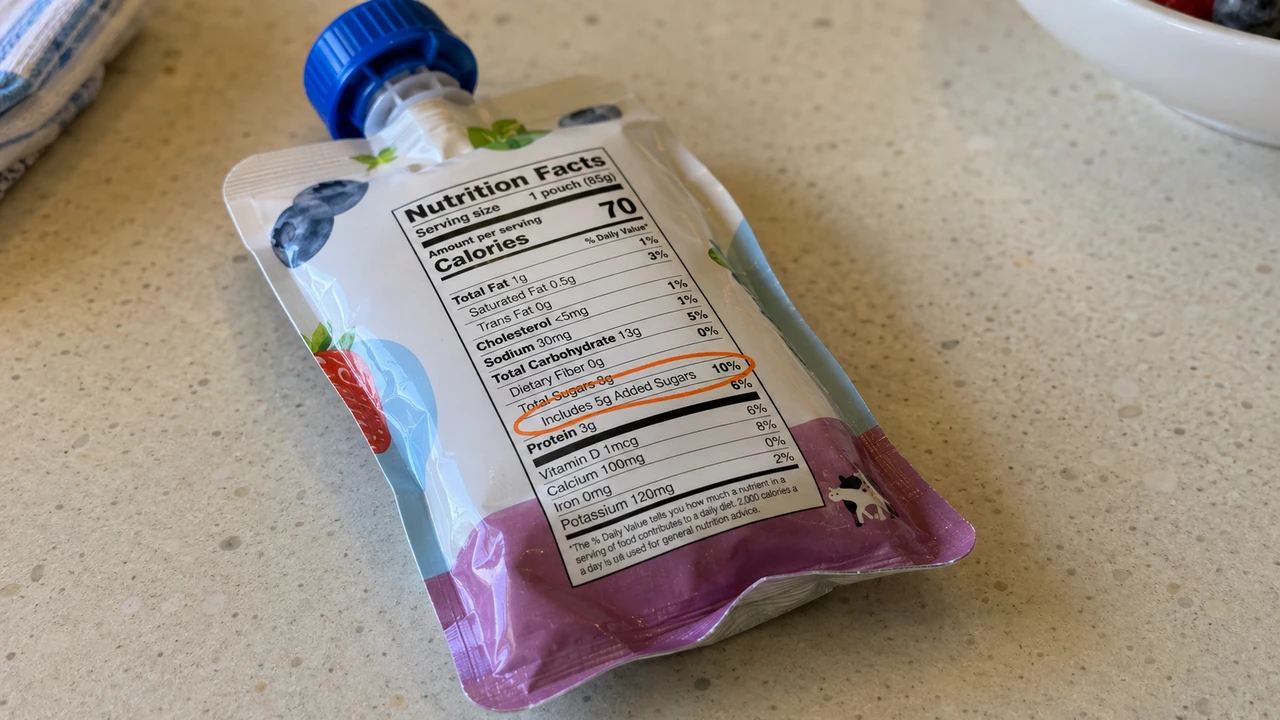 Close-up of a fruit yogurt pouch on a kitchen counter with its Includes Added Sugars line circled in orange